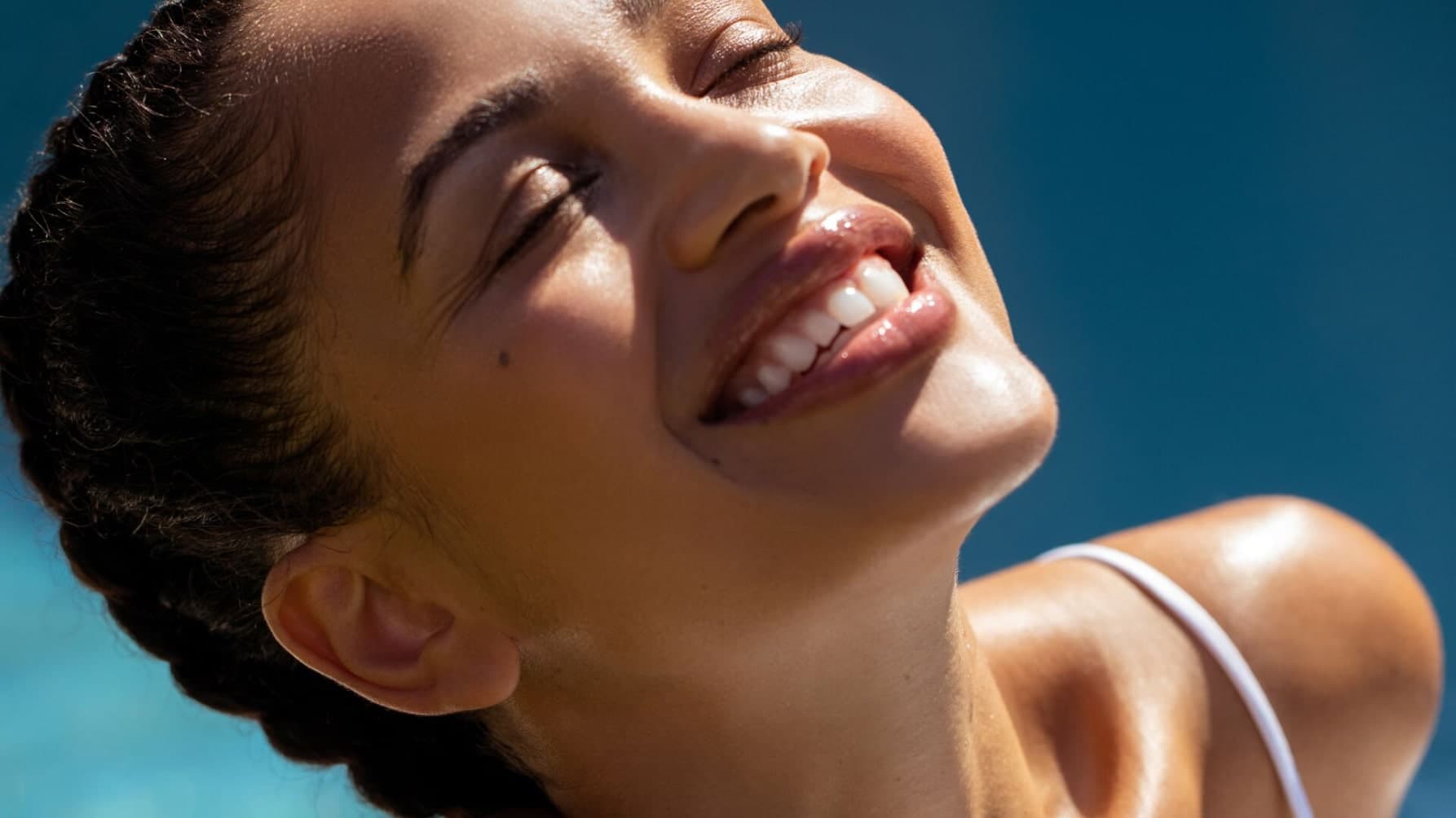 A woman smiles in the sun, eyes closed, enjoying the warmth while protecting her skin from UV damage with selenium.