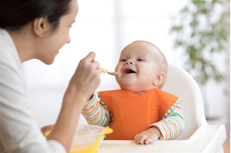 A caregiver gently feeding a baby, illustrating responsive feeding practices.